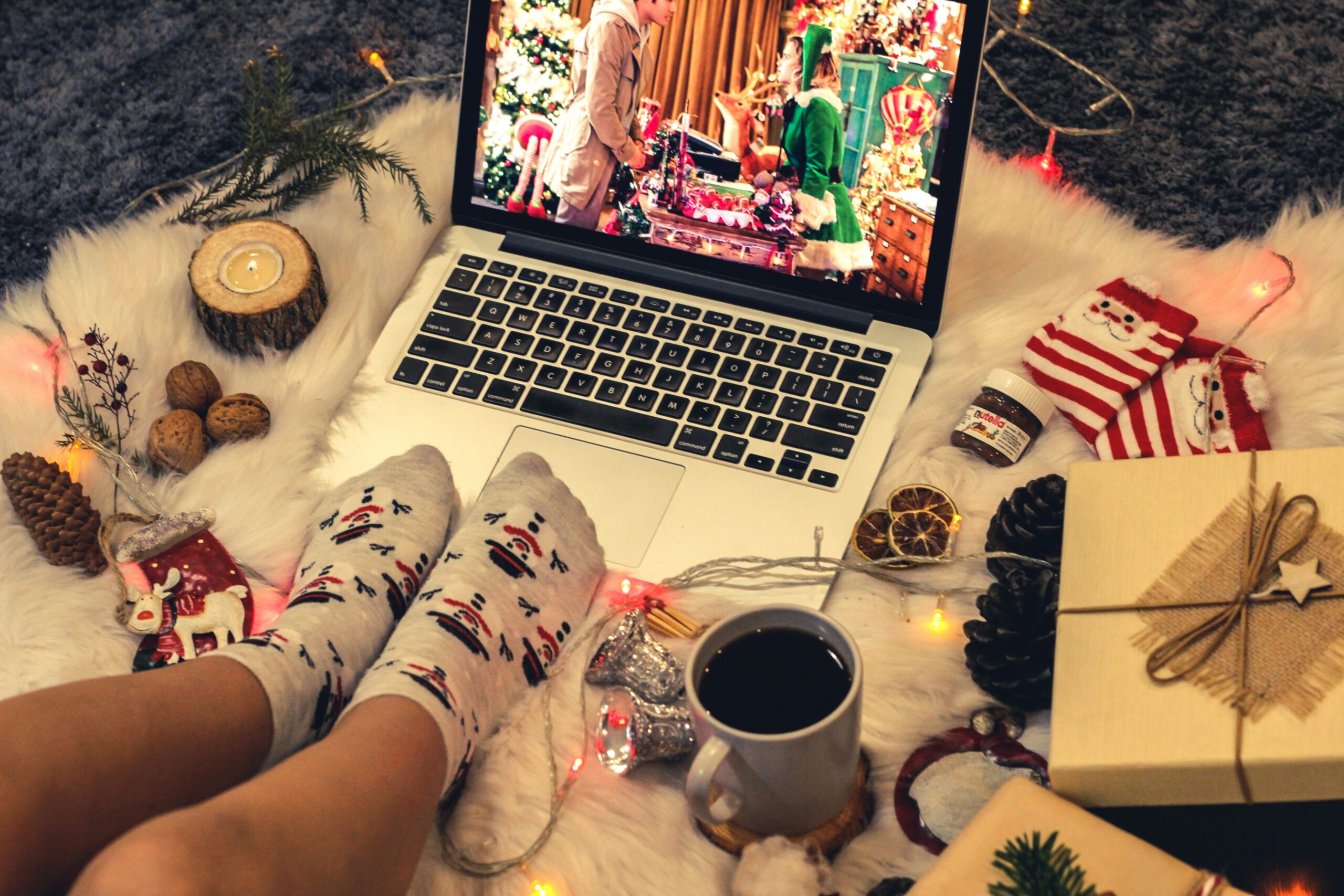 person wearing socks watching Christmas movie on laptop with coffee and ornaments