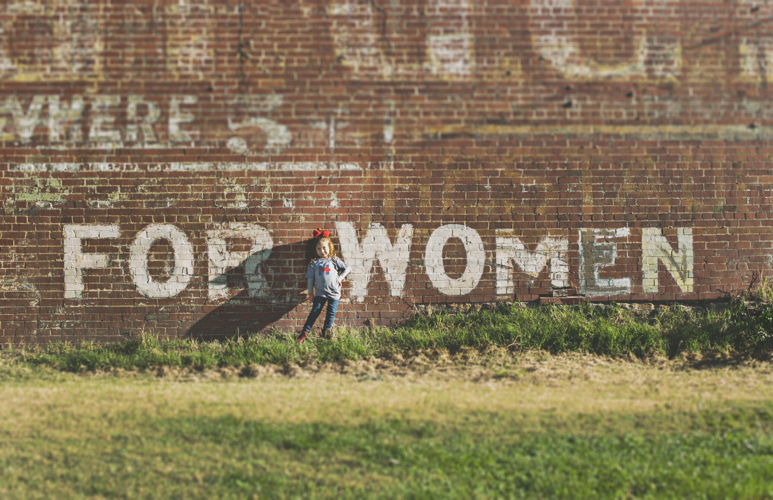for women written on a brown wall with a girl standing in between
