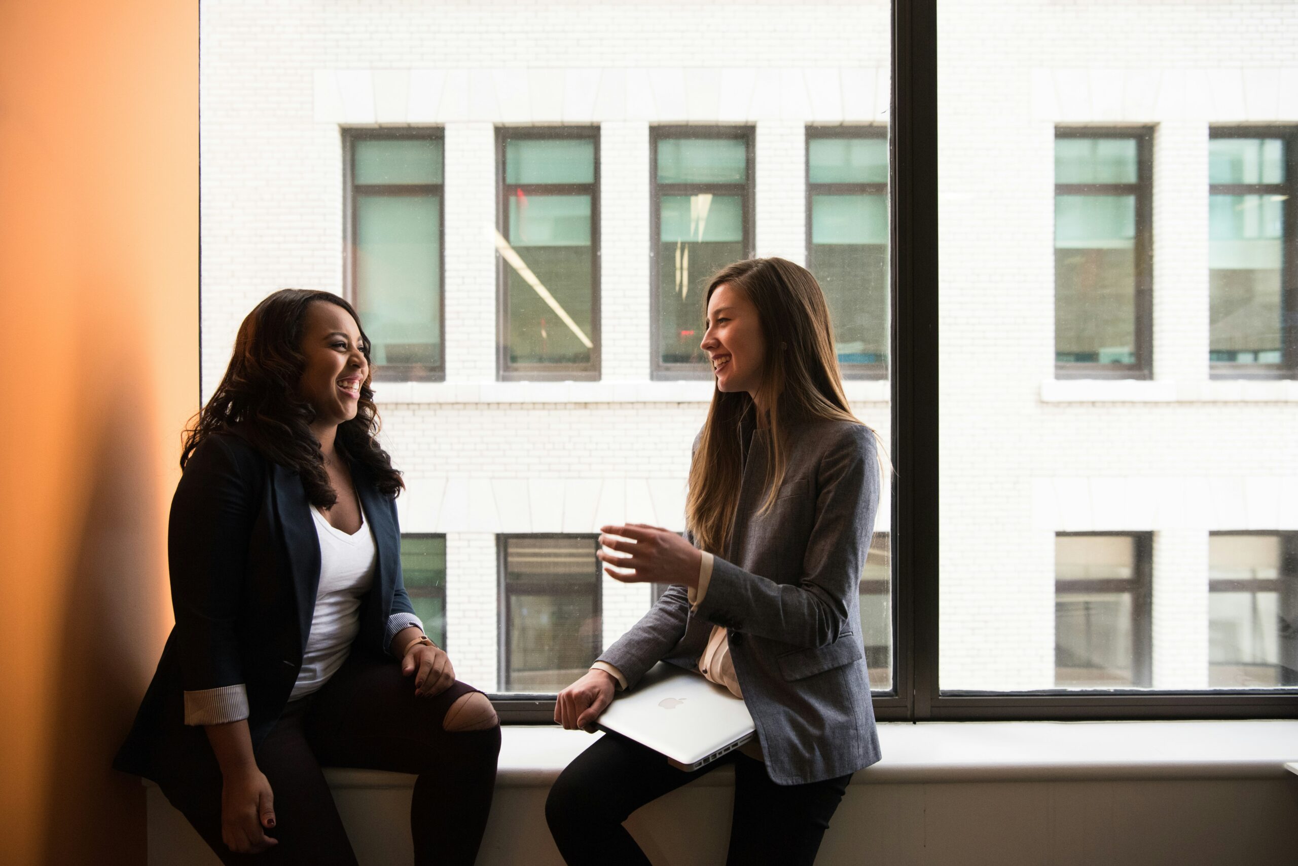 two women in corporate attire sitting by the window